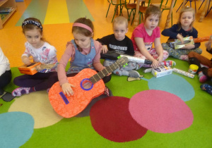 Piątka dzieci gra na instrumentach muzycznych wykonanych wspólnie z rodzicami z materiałów pozyskanych z domowego recyklingu.